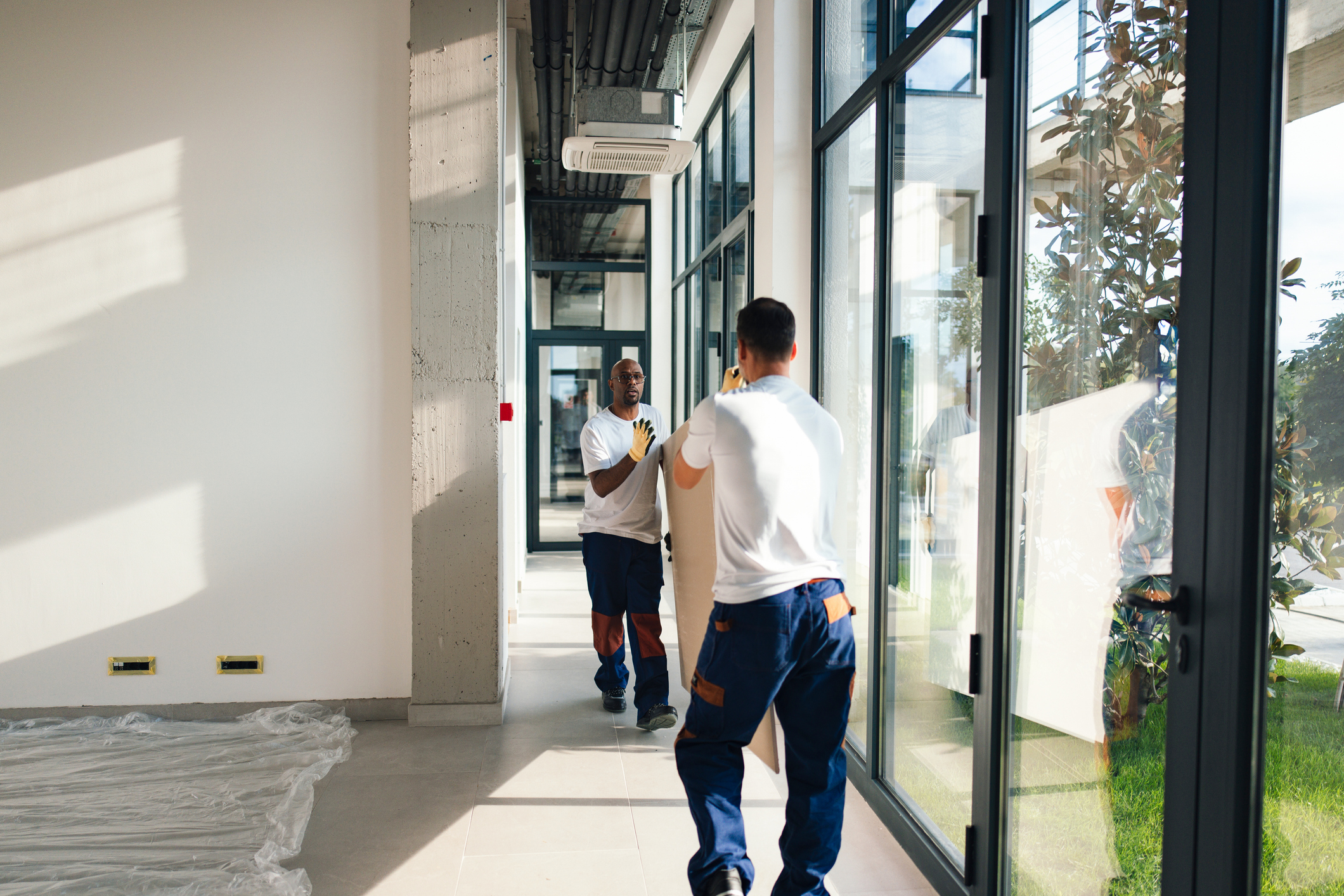 busy construction workers move large panel through bright modern office hallway during daylight renovation